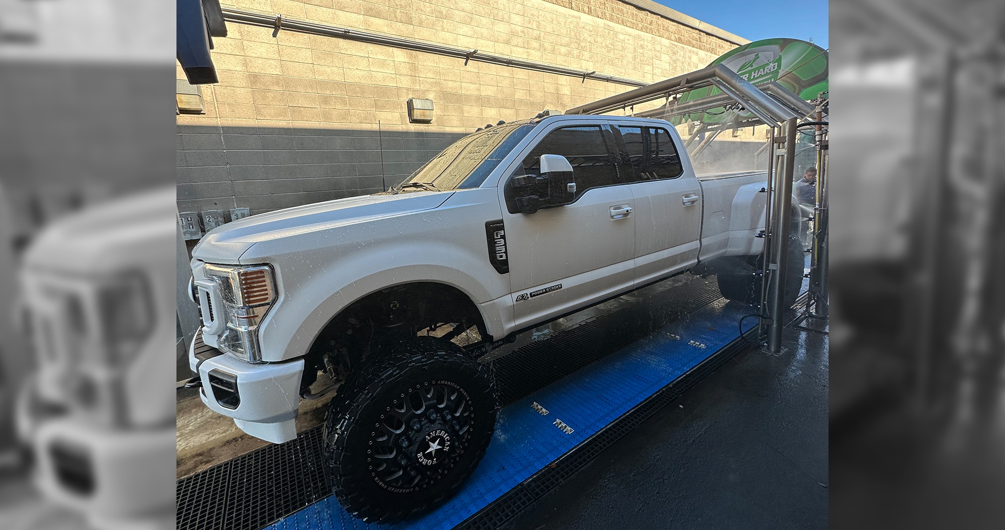 A large lifted Ford Super Duty pickup truck being cleaned at a car wash.