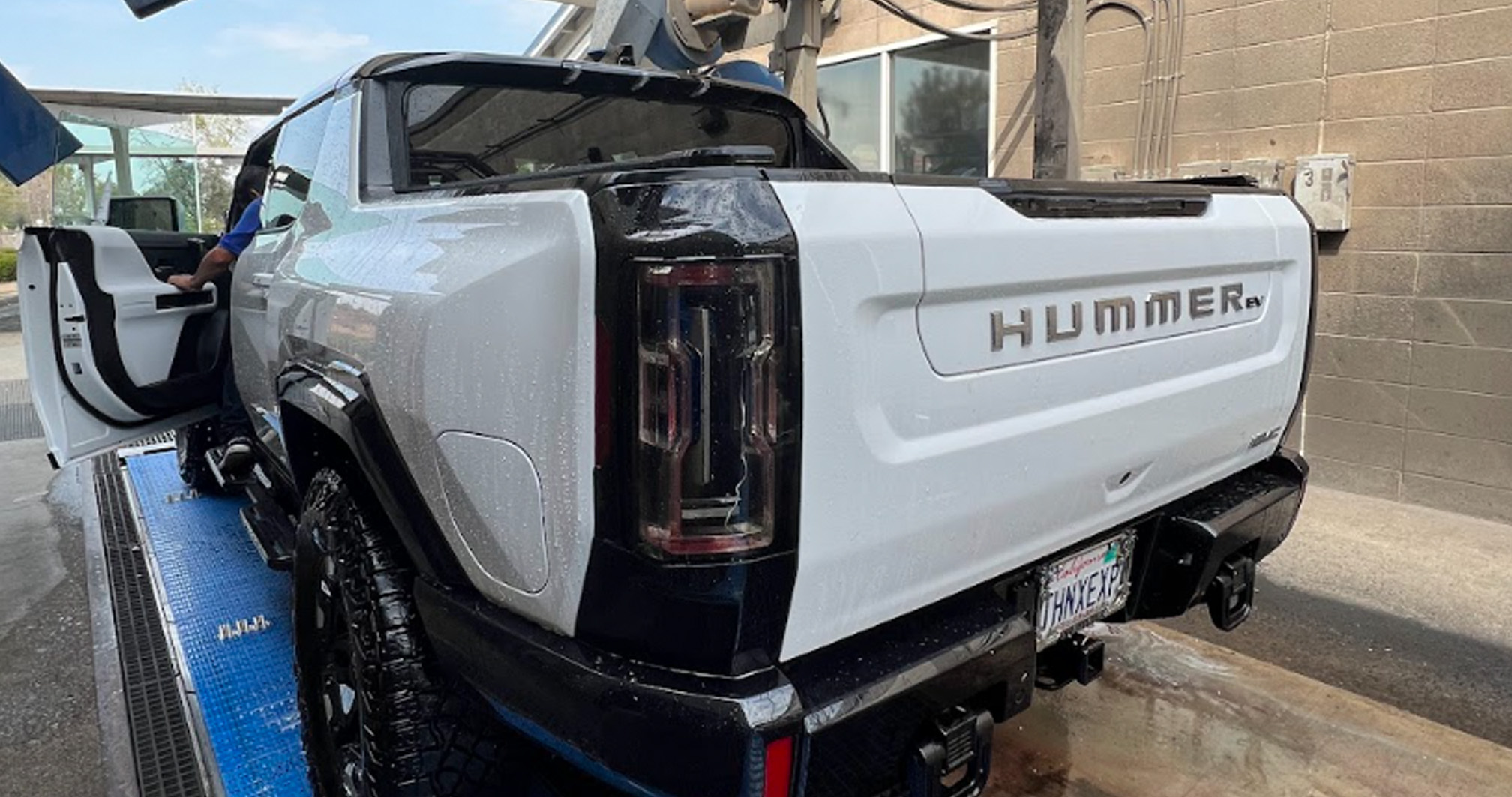 A white Hummer EV undergoing a thorough wash at an automated car wash, with water droplets visible on its surface.