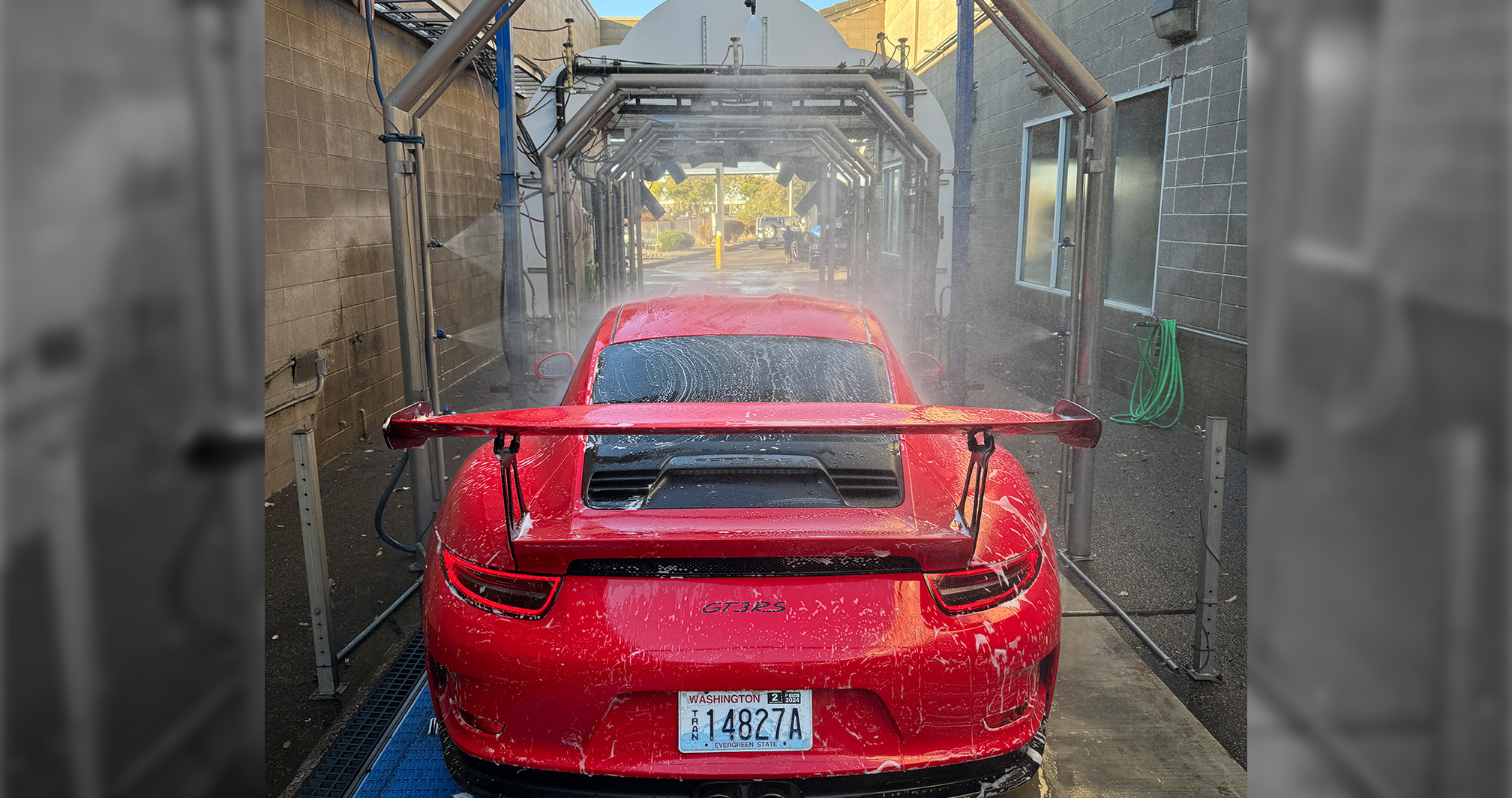A red Porsche GT3 RS going through an automated car wash at Five Star Auto Center, its rear spoiler covered in soap and water.