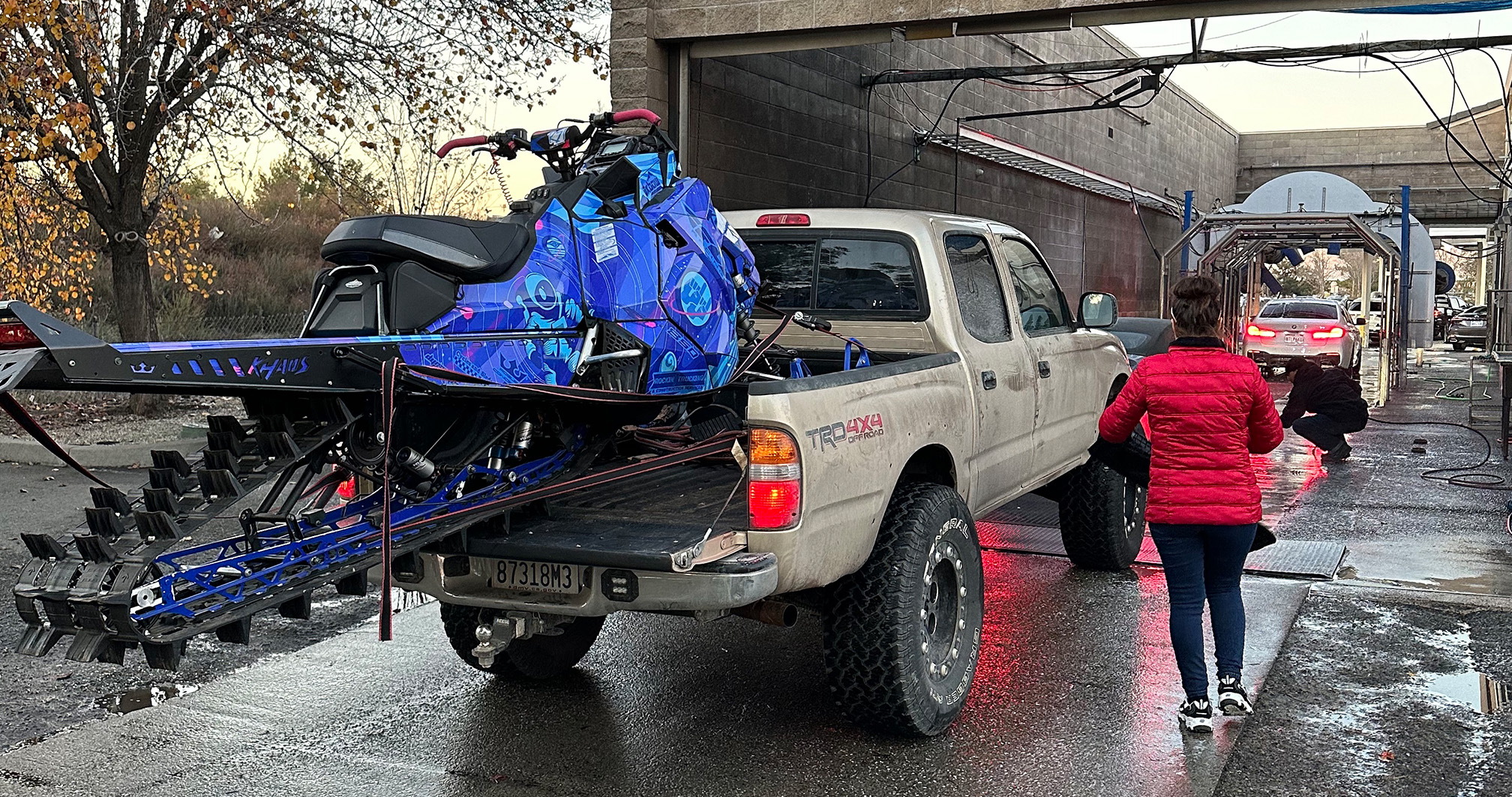 A Toyota Tacoma with a vibrant blue snowmobile strapped to the bed, waiting in line at the car wash.
