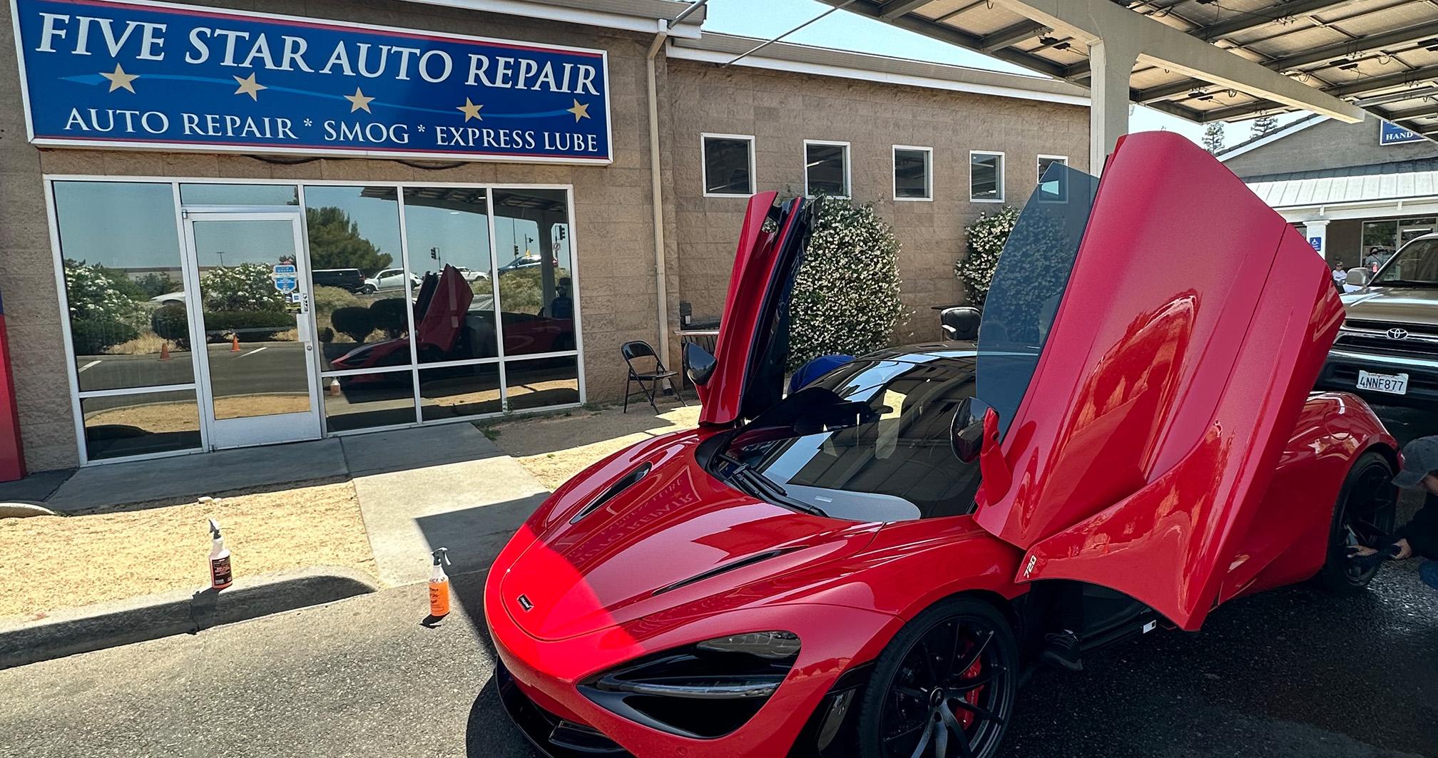 A striking red McLaren 720S with butterfly doors open, parked outside a Five Star Auto Repair shop.